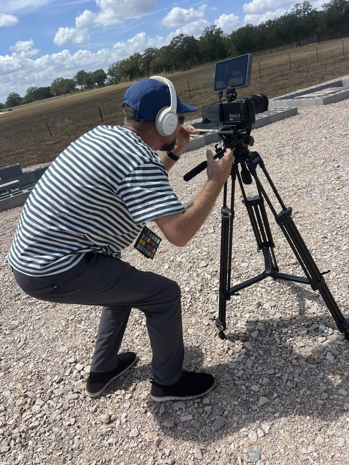 Camera operator crouched behind the tripod with headphones on and a color chart in hand