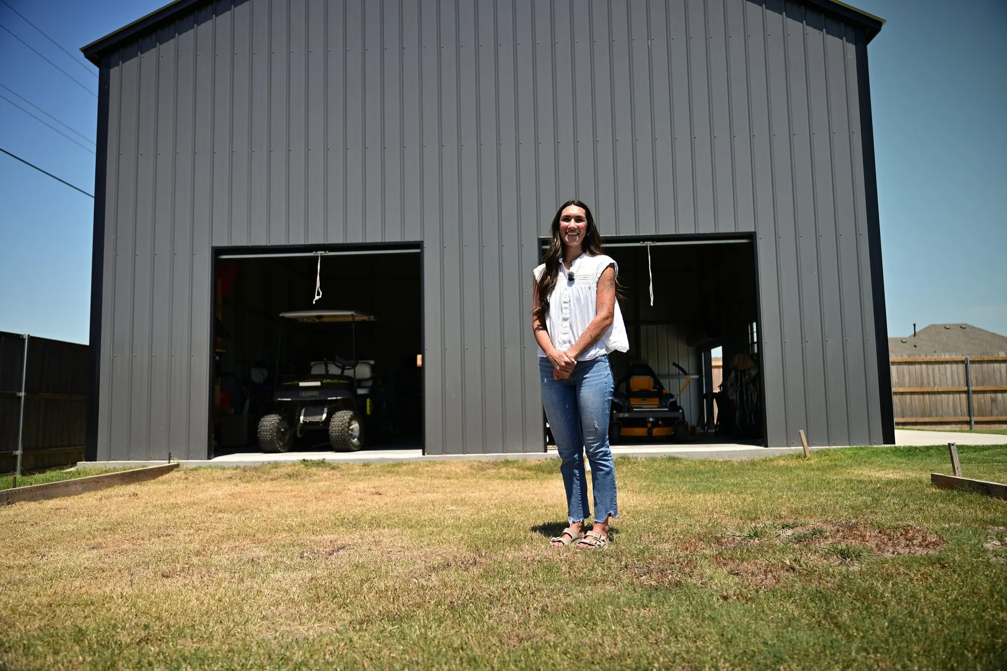 Brittany standing in front of the open roll-up doors of the custom metal shop, golf cart parked inside