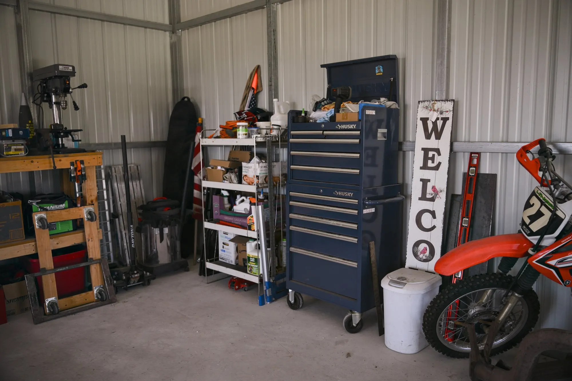 Inside the workshop: tool chest, welcome sign, and a kids dirt bike against the metal wall