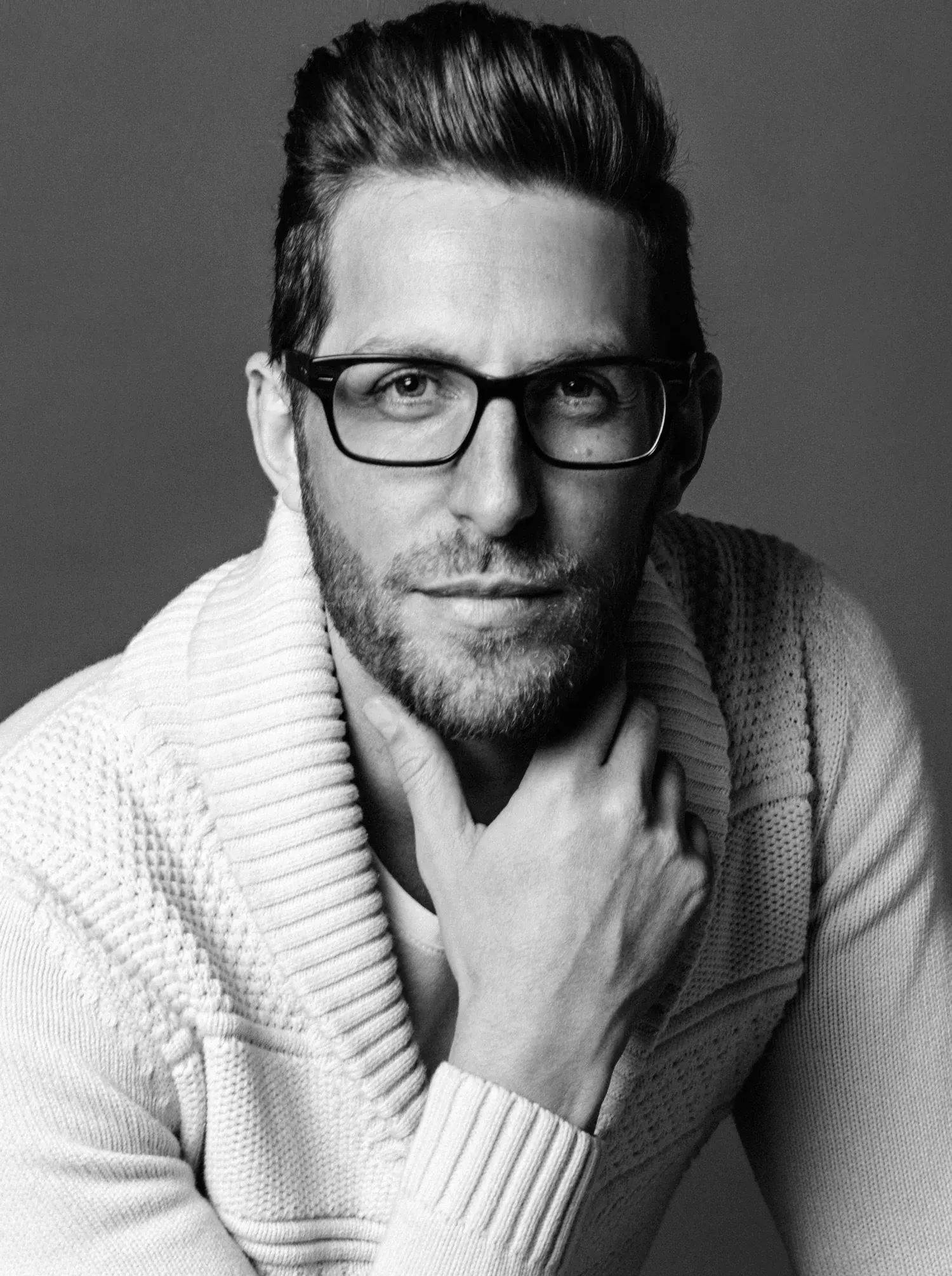 Black-and-white Dallas corporate headshot of a bearded man in glasses and a white knit sweater, hand at his chin