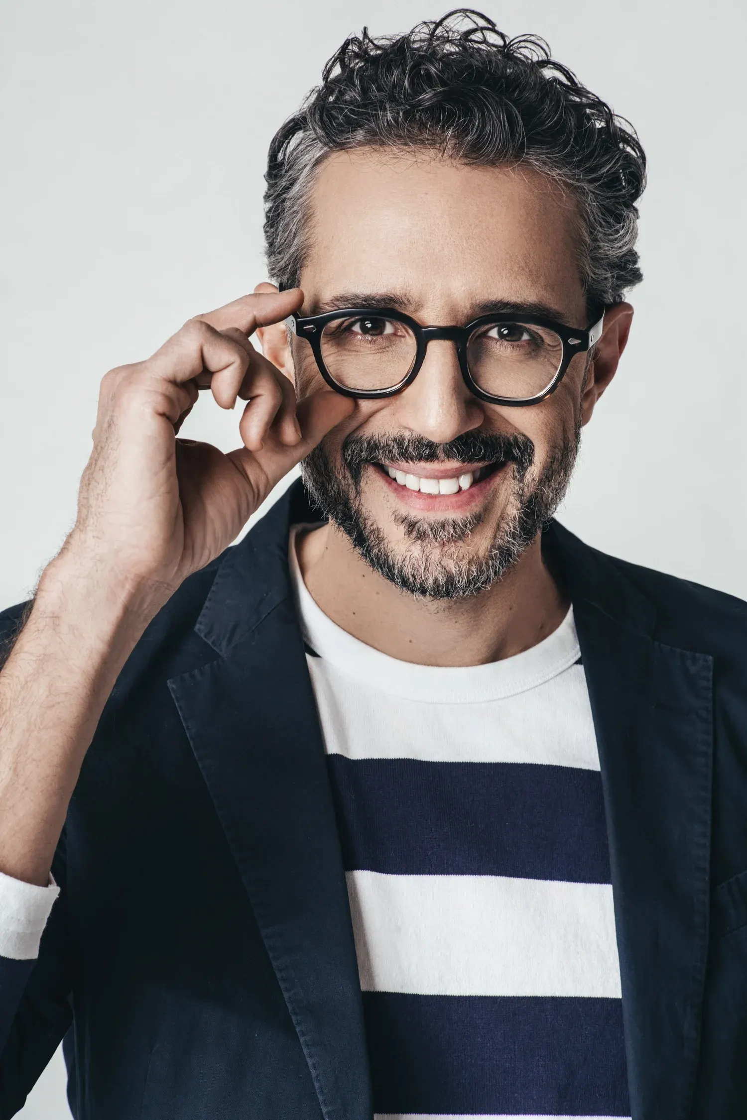 Dallas corporate headshot of a smiling man with gray hair adjusting his glasses, in a striped shirt and dark jacket on a gray backdrop