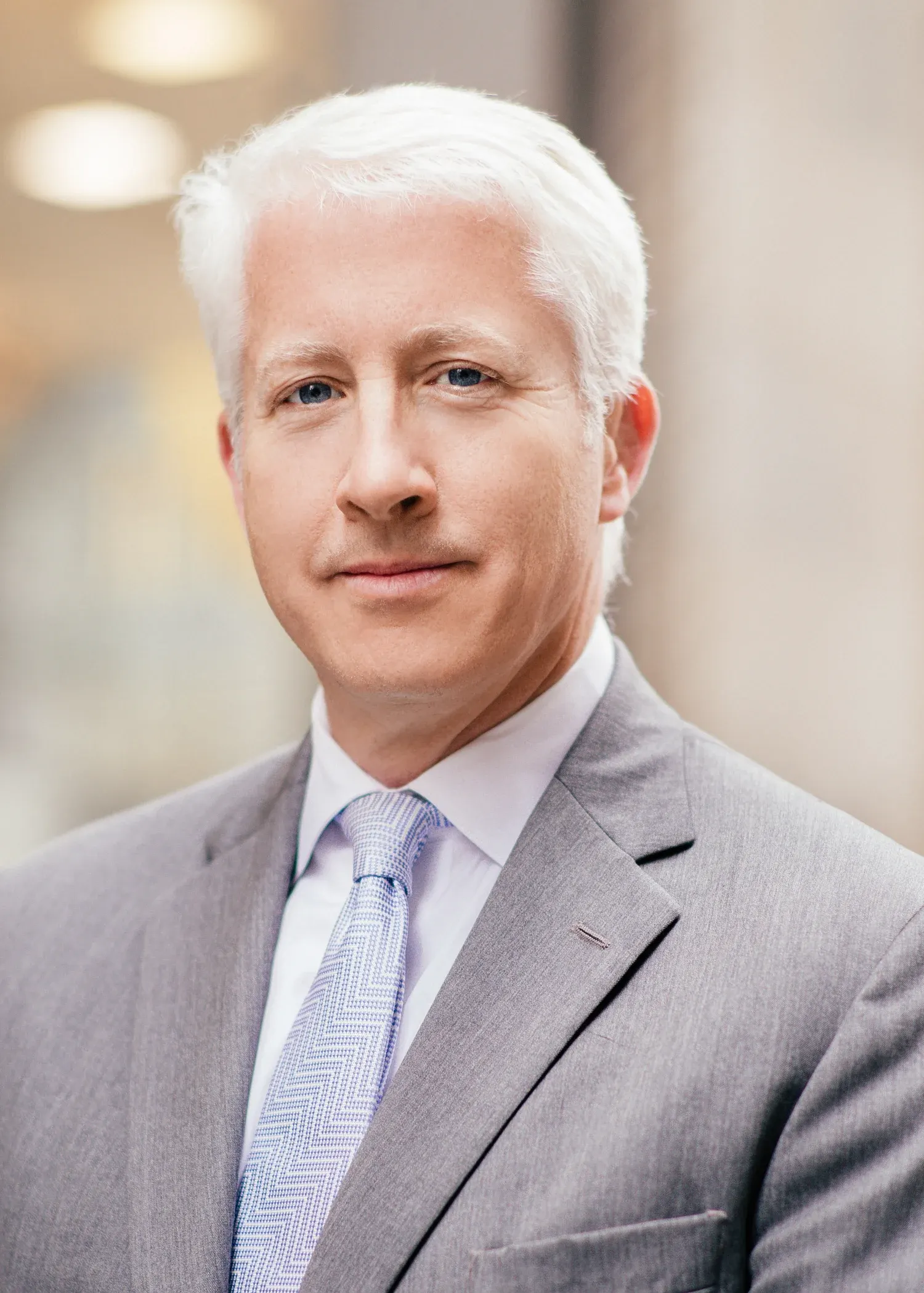 Dallas corporate headshot of a silver-haired man in a gray suit and lavender tie with a softly blurred office behind him
