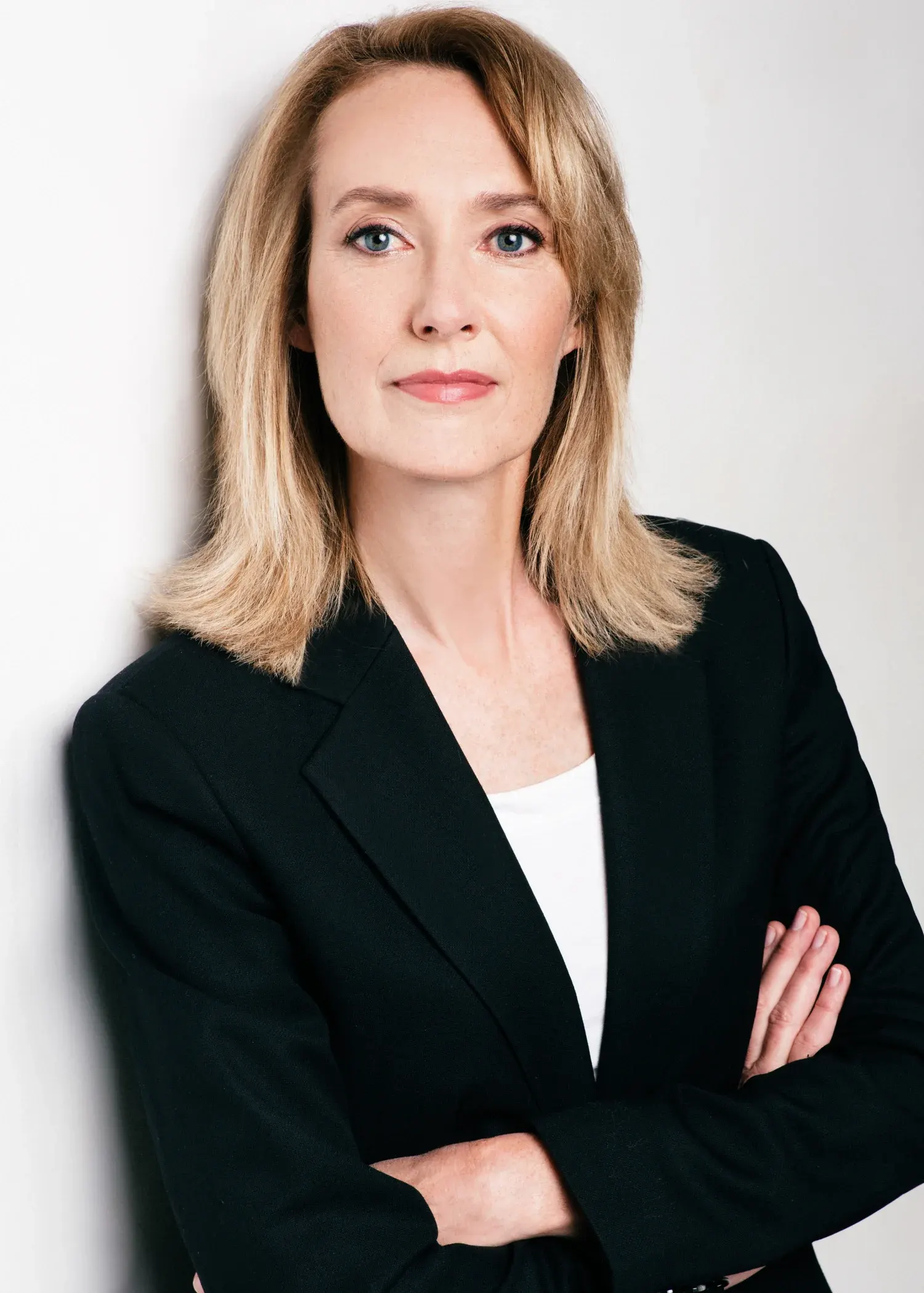 Professional headshot of a woman with shoulder-length blonde hair in a black blazer and white top on a white backdrop
