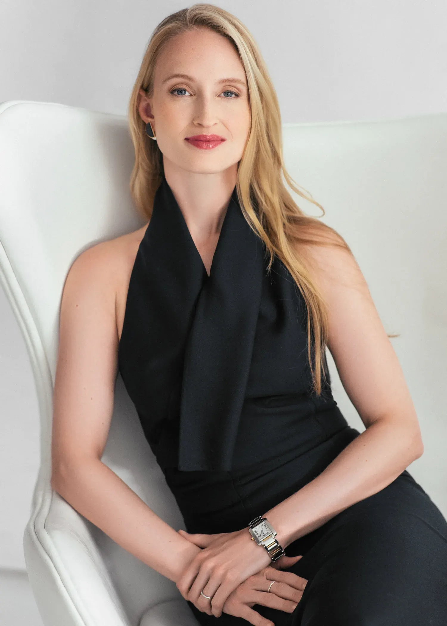 Seated portrait of a woman with long blonde hair in a black halter top on a white chair against a white backdrop