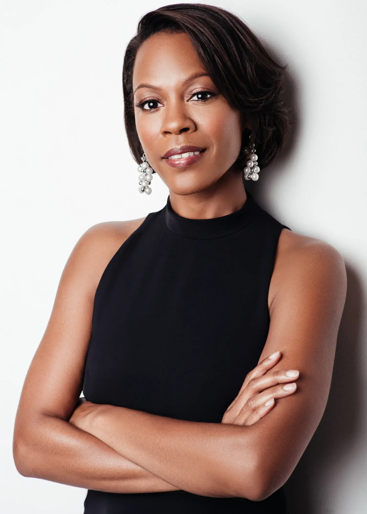 Dallas corporate headshot of a woman in a black sleeveless top with arms crossed against a gray studio backdrop