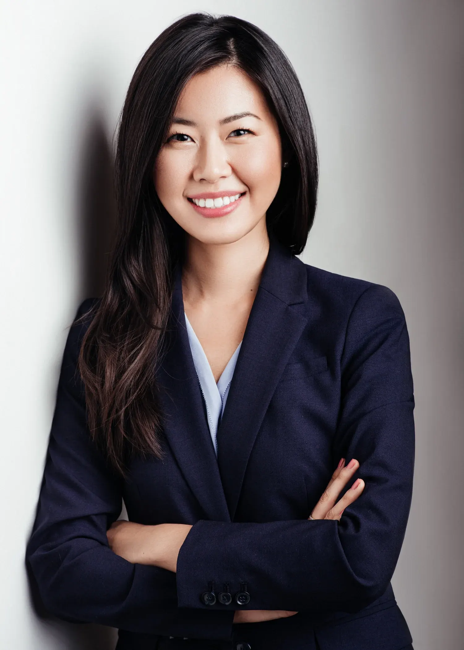 Dallas team headshot of a smiling woman in a navy blazer and light blue shirt with arms crossed on a white backdrop