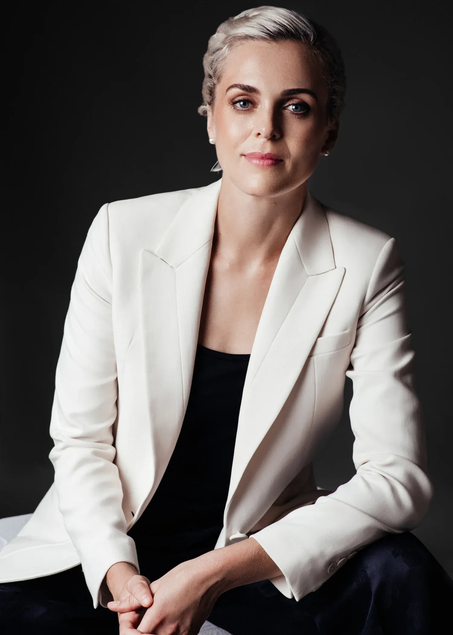 Seated executive portrait of a woman with short blonde hair in a white blazer against a gray studio backdrop