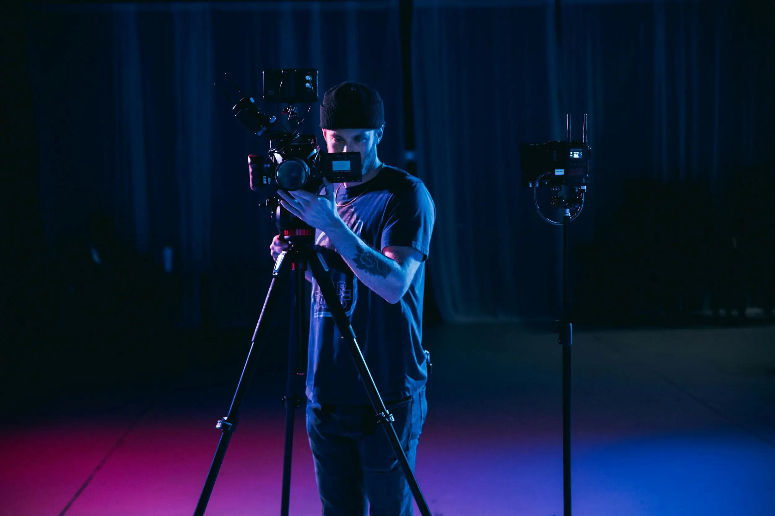 Camera operator framing a shot on a cinema camera in a studio lit with blue and pink light