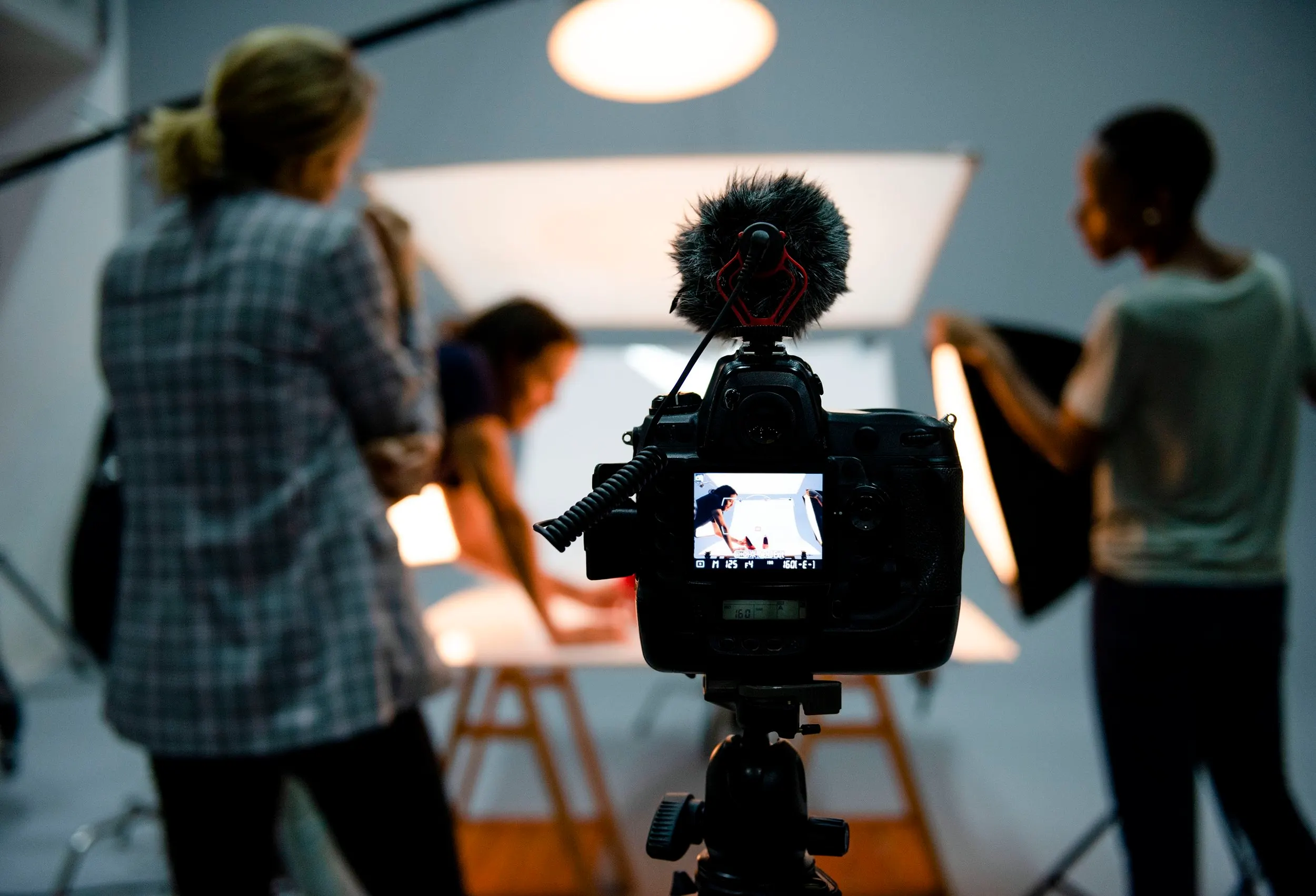 Video camera with shotgun microphone recording a studio shoot behind the scenes