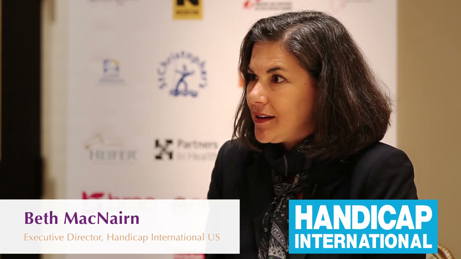 Beth MacNairn, executive director of Handicap International US, interviewed in front of a humanitarian event backdrop
